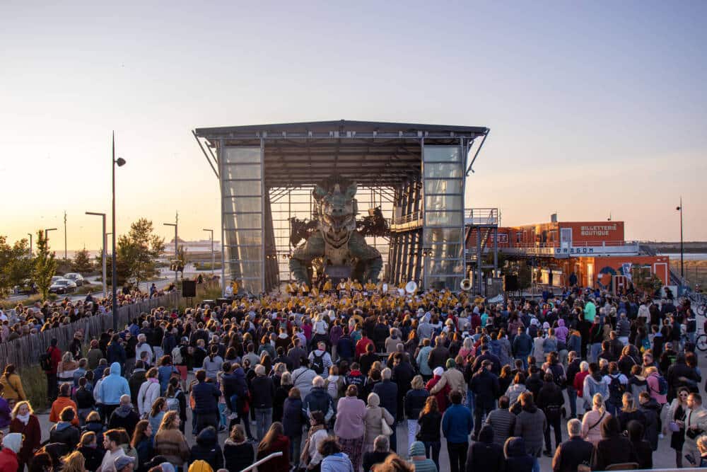 Sur cette photo prise en recul de l'abri du Dragon de Calais, on voit une foule de spectateur profiter d'un concert à la lumière tombante du jour.