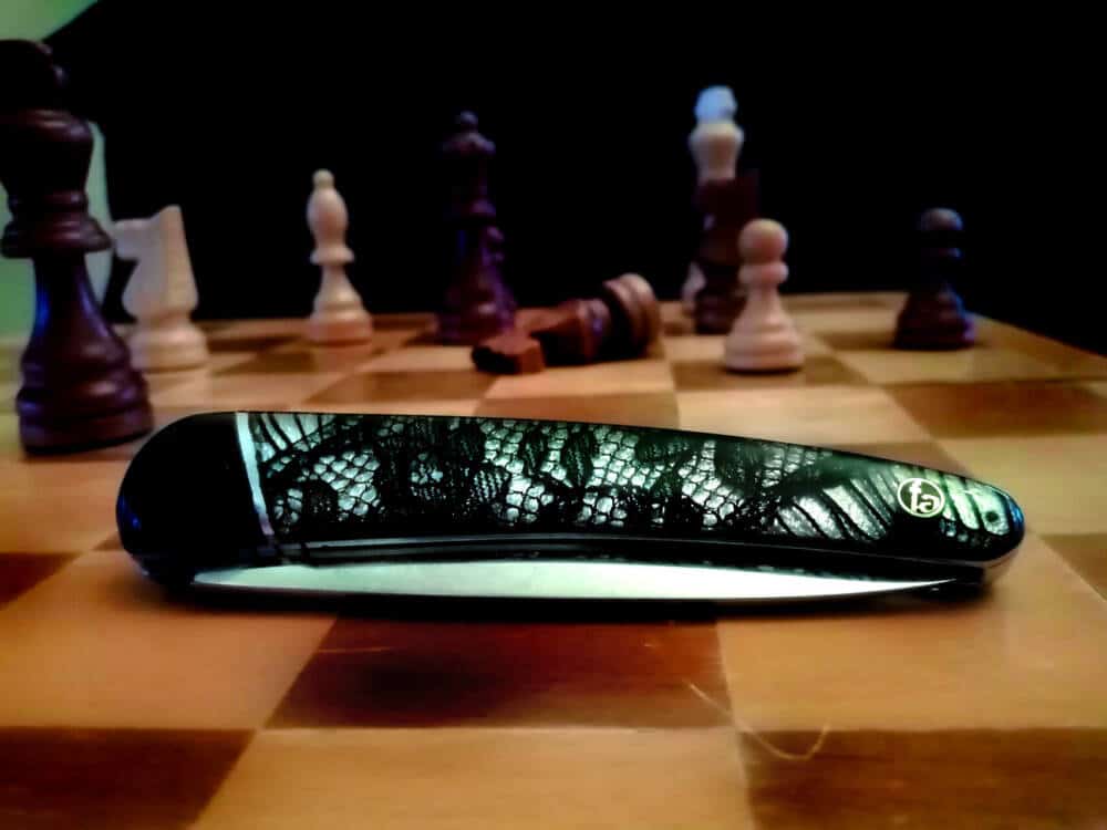 Gros plan sur le couteau le calaisien dont le manche est incrusté de dentelle et posé sur un plateau de jeu d'échecs.