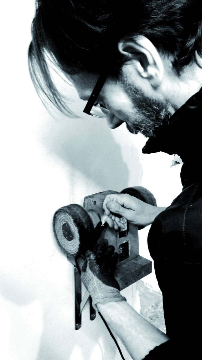 Portrait tn noir et blanc de Franck Ackermann qui affute un couteau sur sa meuleuse.