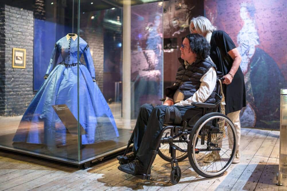 Deux visiteurs des collections permanentes de la Cité de la Dentelle, dont l'une est en fauteuil roulant.