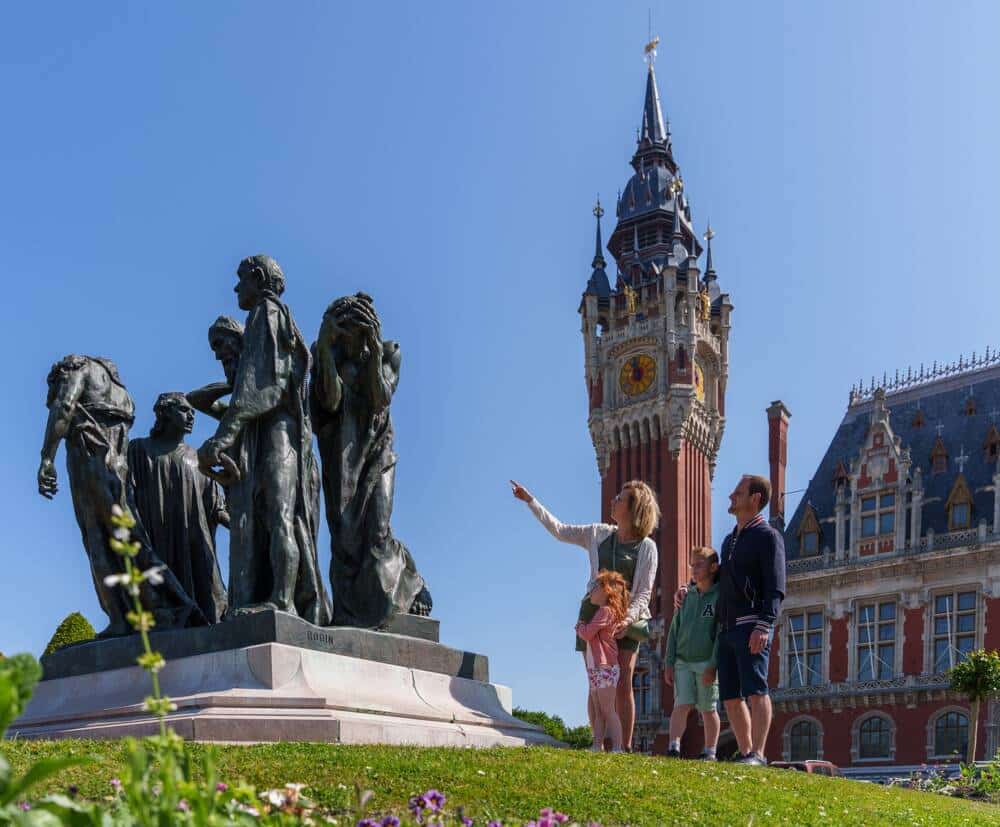 Une famille au pied du monument aux Bourgeois de Calais avec l'Hôtel de ville de Calais en arrière-plan.