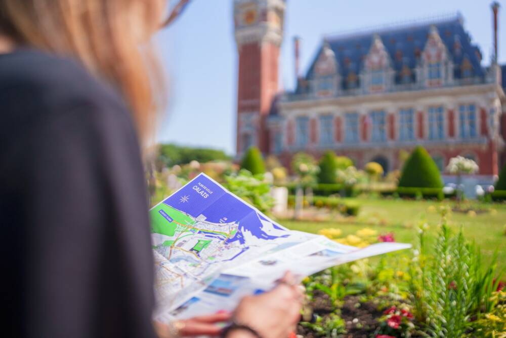 Personne au pied de l'hôtel de ville de Calais se repérant à l'aide de la Carte Calais XXL.