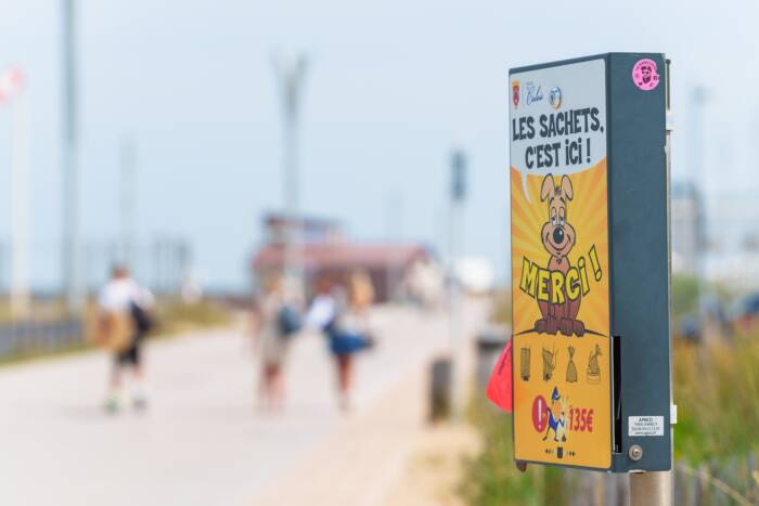 Panneau de sensibilisation hygiène des chiens sur le front de mer de Calais avec la jetée en arrière-plan.