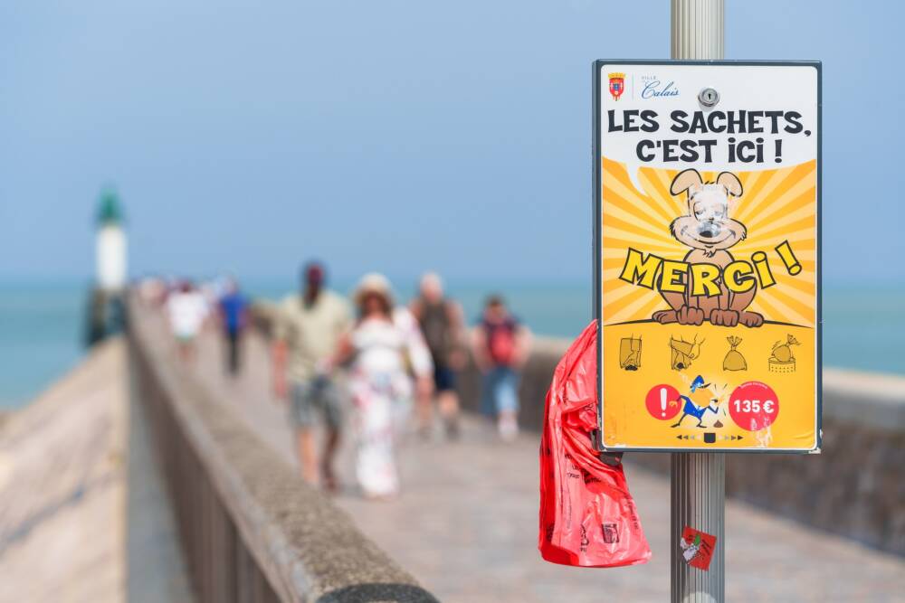 Panneau de sensibilisation hygiène des chiens sur le front de mer de Calais avec la jetée en arrière-plan.