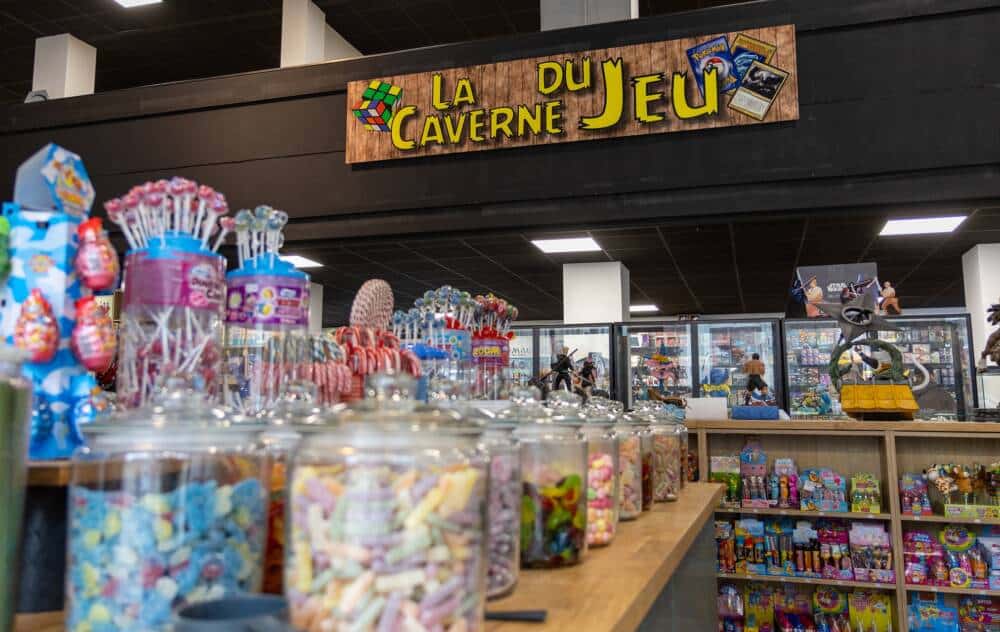 Rayon bonbons et sucreries avec enseigne La Caverne du Jeu en arrière-plan.